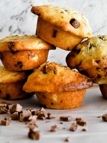 banana choc chip muffins stacked with choc chips scattered in foreground