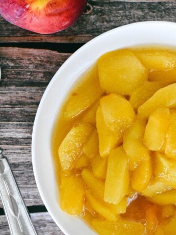 Stewed peaches in bowl on timber table with silver spoon at side.